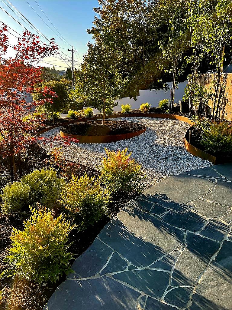 Corten steel ring and curved beds in white gravel beside crazy paving