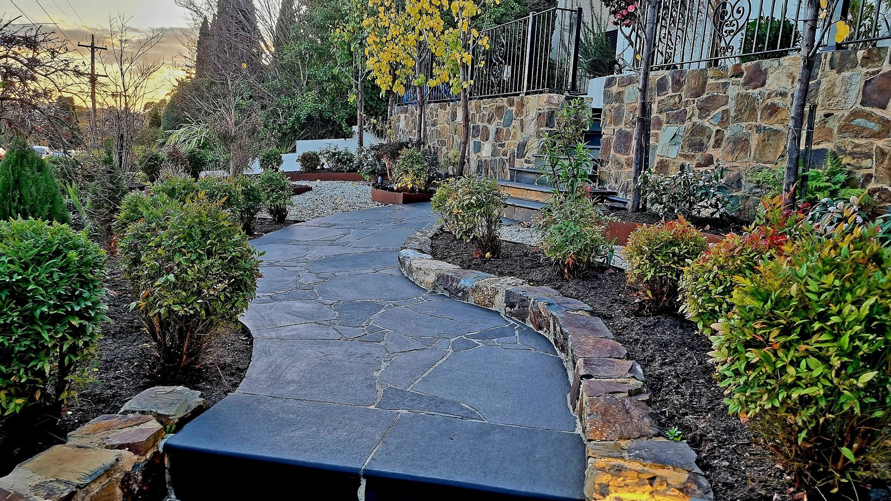 Curving stone crazy paving path edged with a natural stone wall at sunset
