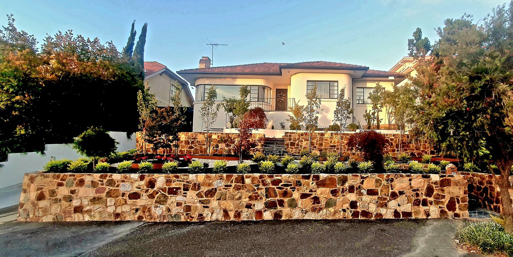 Art Deco house above a natural stone front wall and terraced garden at sunset