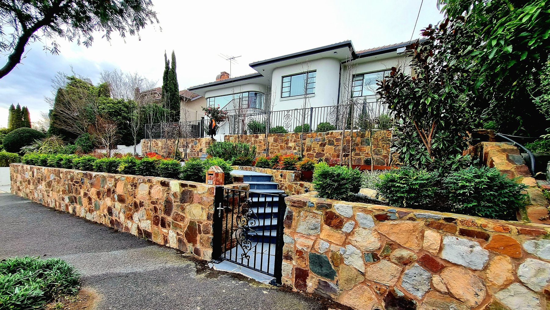 Natural stone front wall, iron gate and stone steps up to the Art Deco house