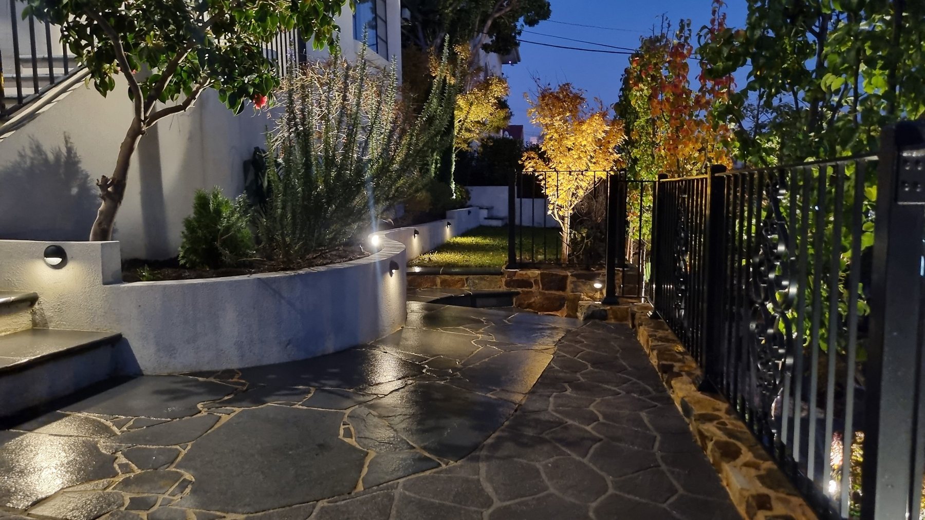 Crazy paving side path and curved planter with step lights at night