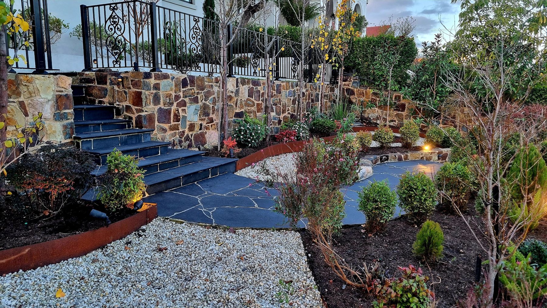 Black stone steps, crazy paving and Corten edged beds below the stone wall