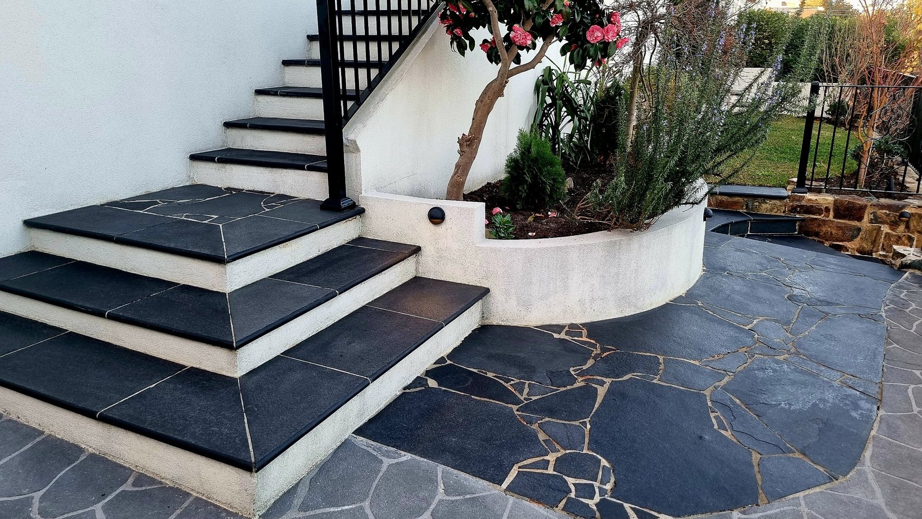 Black stone treads on white rendered steps beside a curved planter and crazy paving