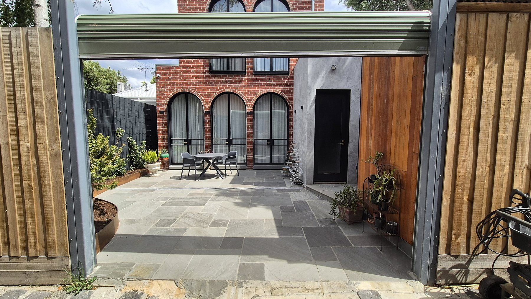 Courtyard seen through the rear gate, with arched windows, stone paving and a cedar shed