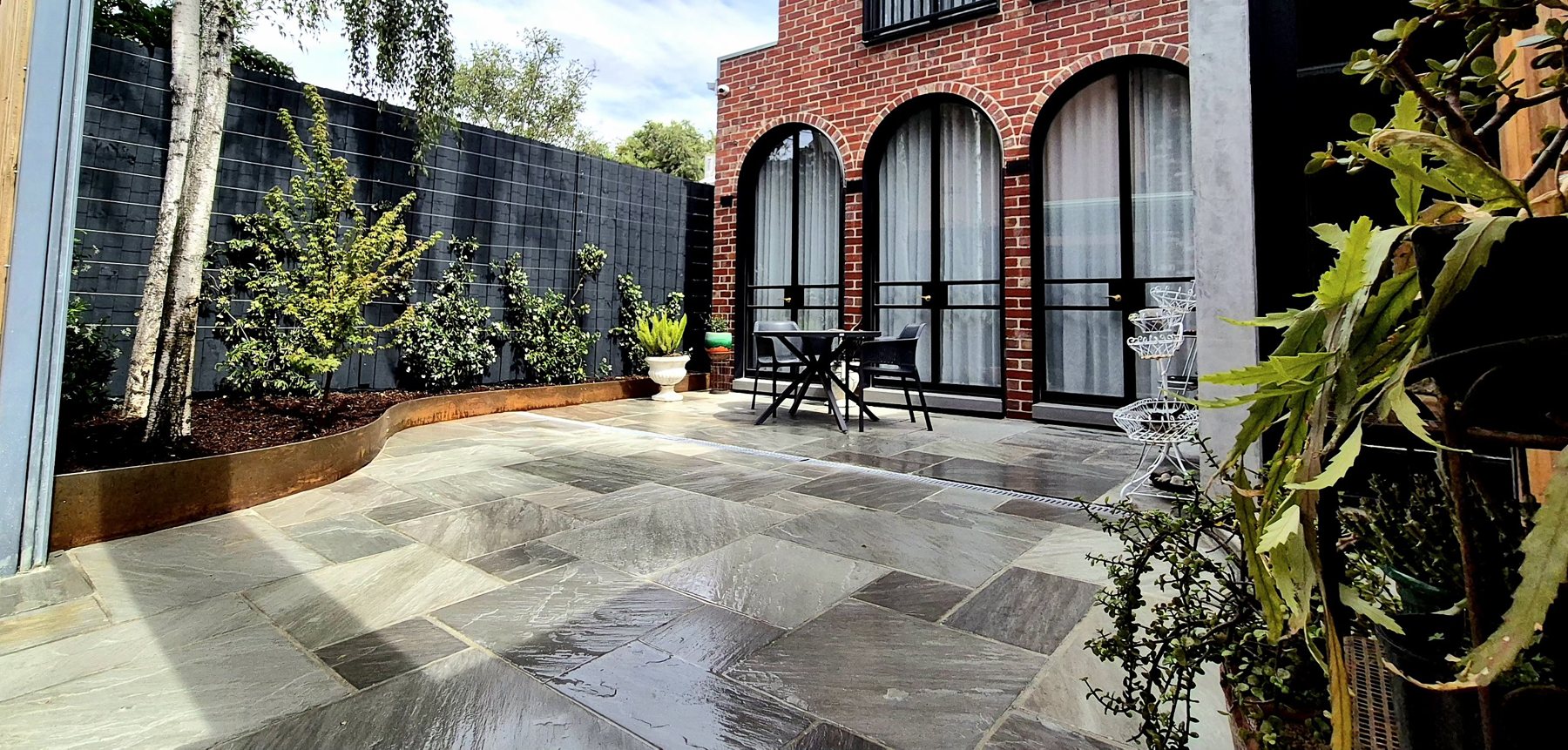 Stone paving sweeping past the Corten bed to the dining area under the arches