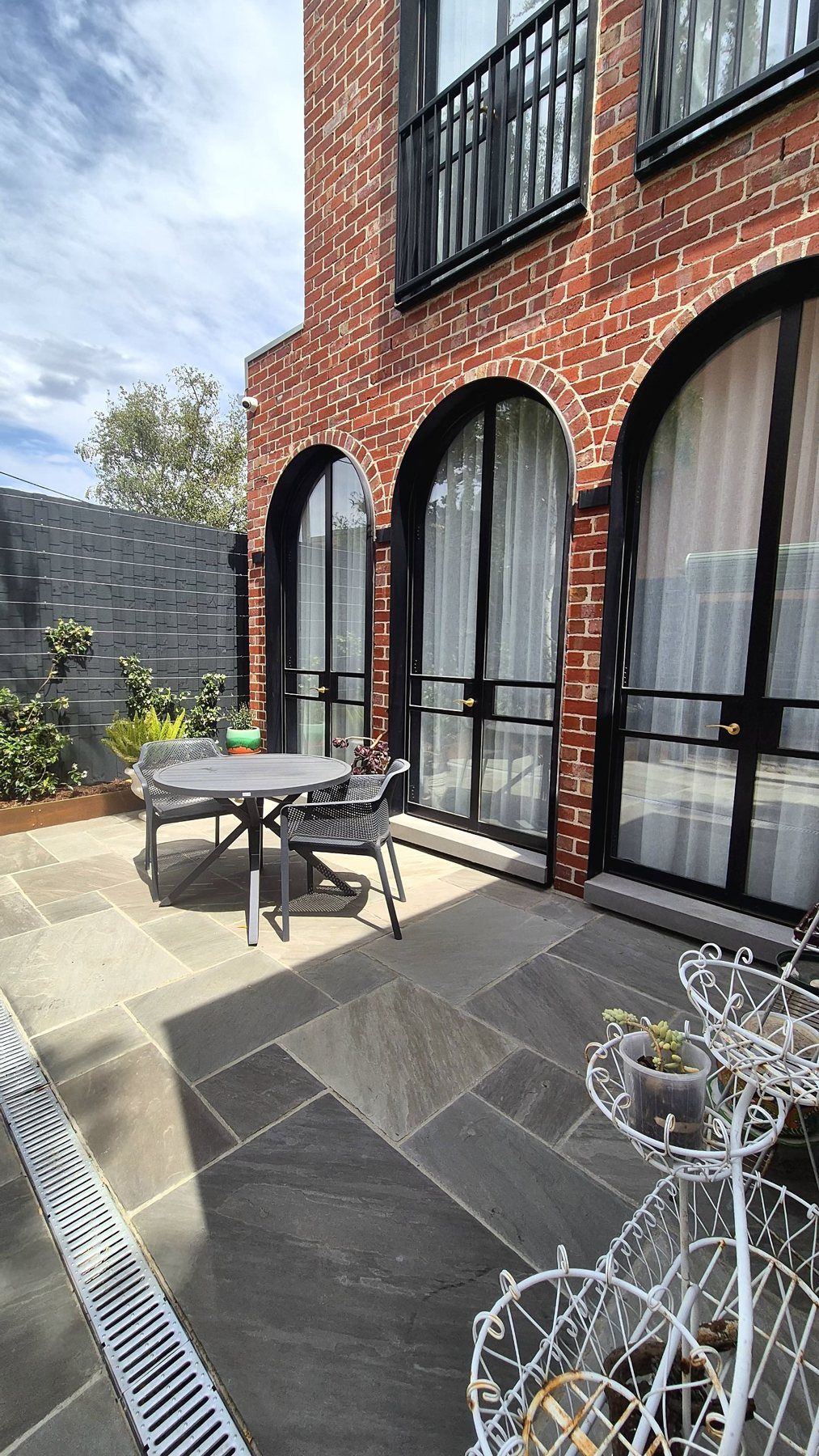 Dining setting on stone paving beneath arched black windows
