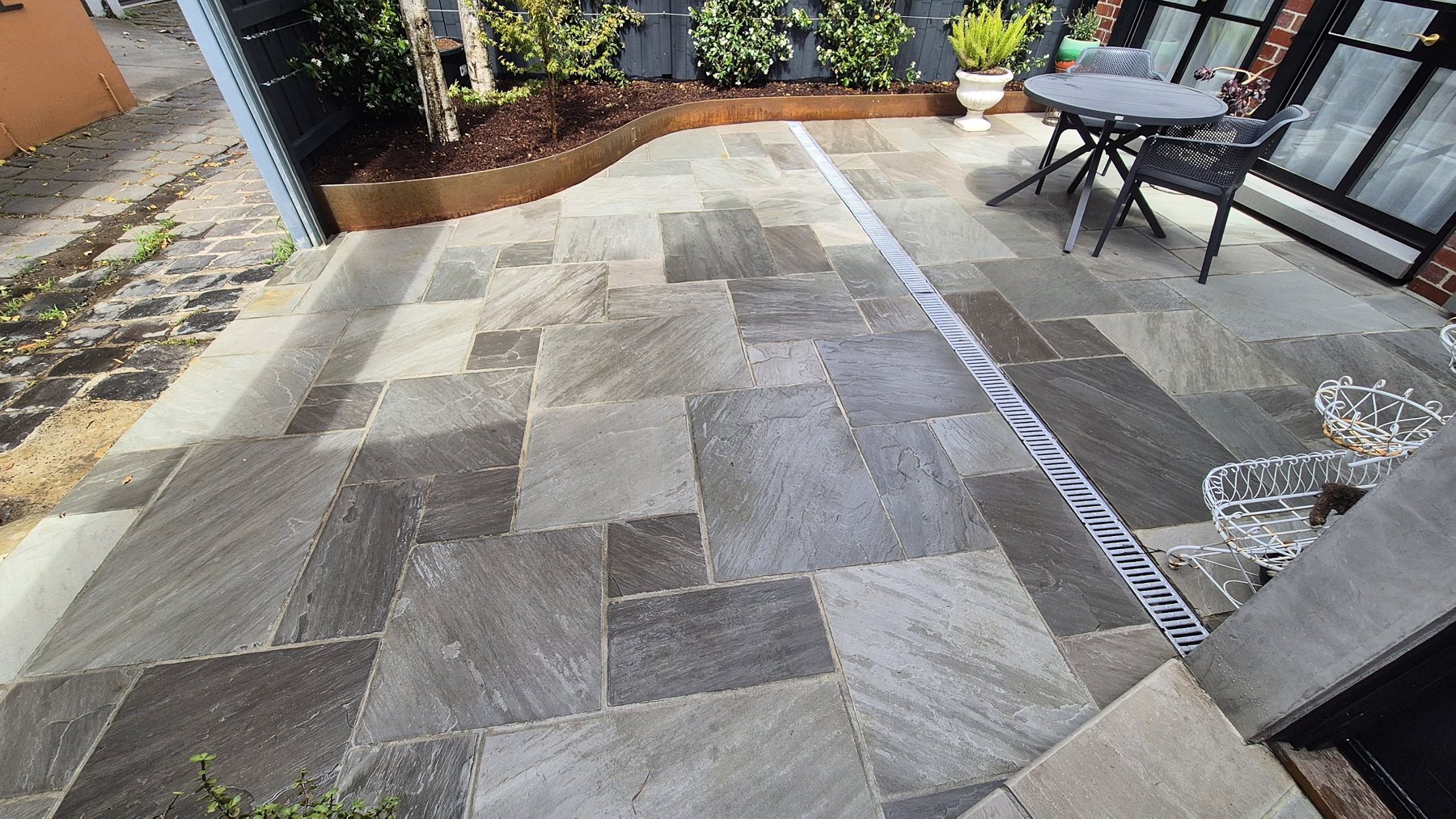 Stone paving with a strip drain beside the Corten bed