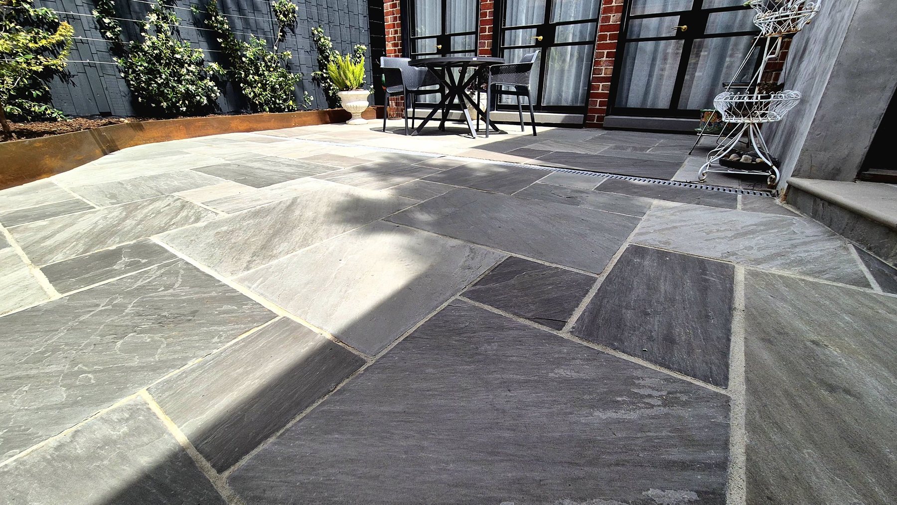 Low view across the stone paving to the dining table and jasmine fence