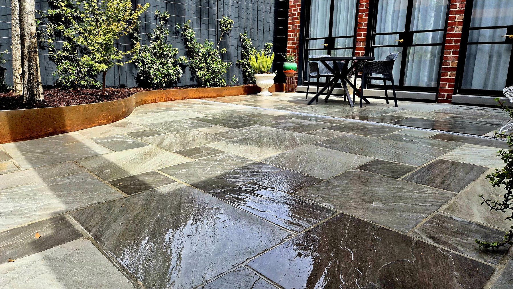 Wet stone paving and the curved Corten edge in sunlight
