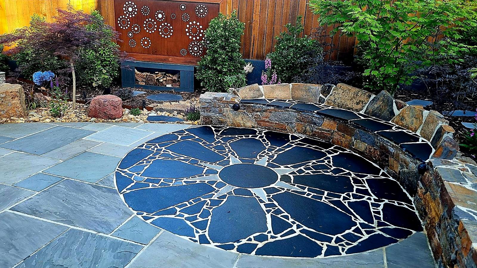 Eight-point sun in Black Beauty limestone set into grey limestone paving, beside a curved natural stone seat wall