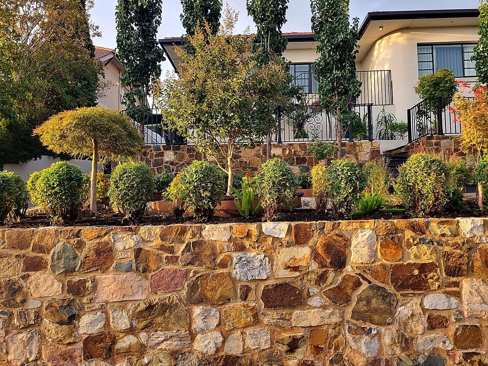 Long natural stone retaining wall in golden evening light below an Art Deco house