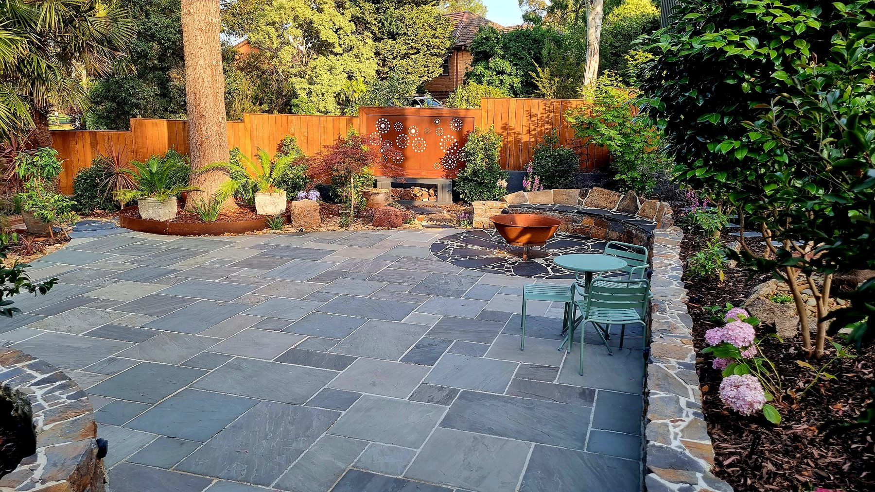 Stone paved courtyard with fire pit circle, curved seat wall, Corten screen and timber fence