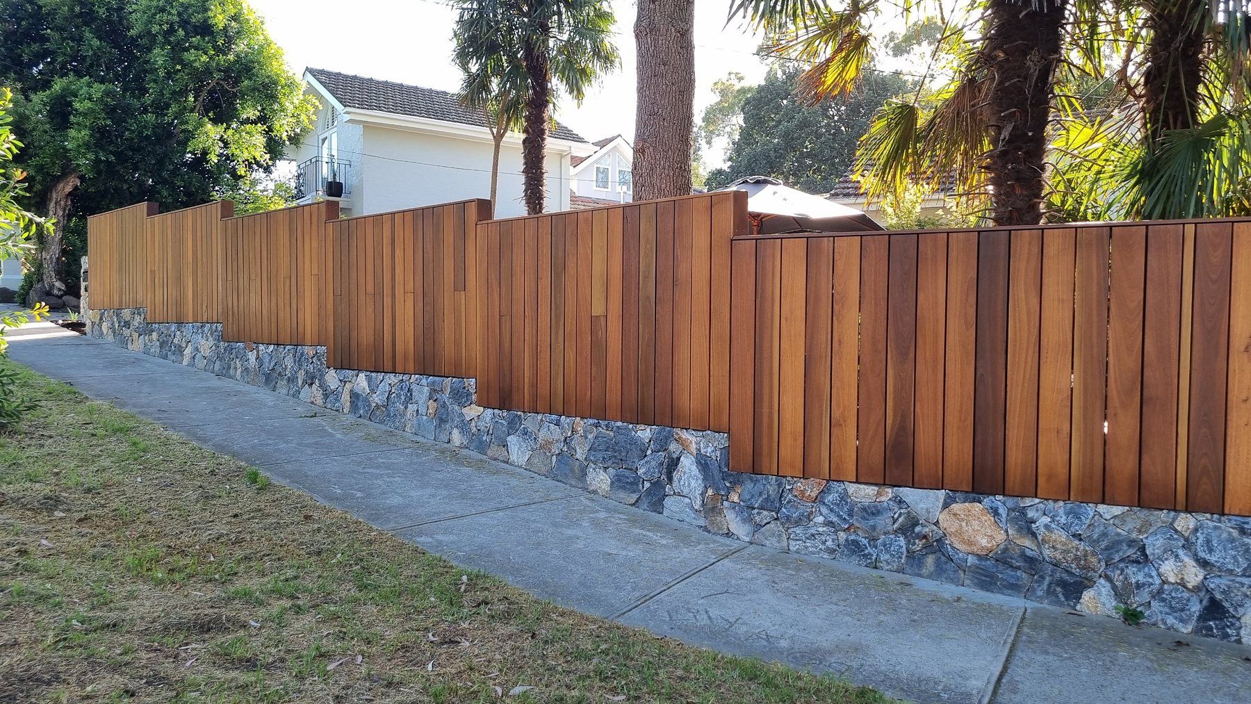 Hardwood batten fence stepping down the street over a natural stone plinth