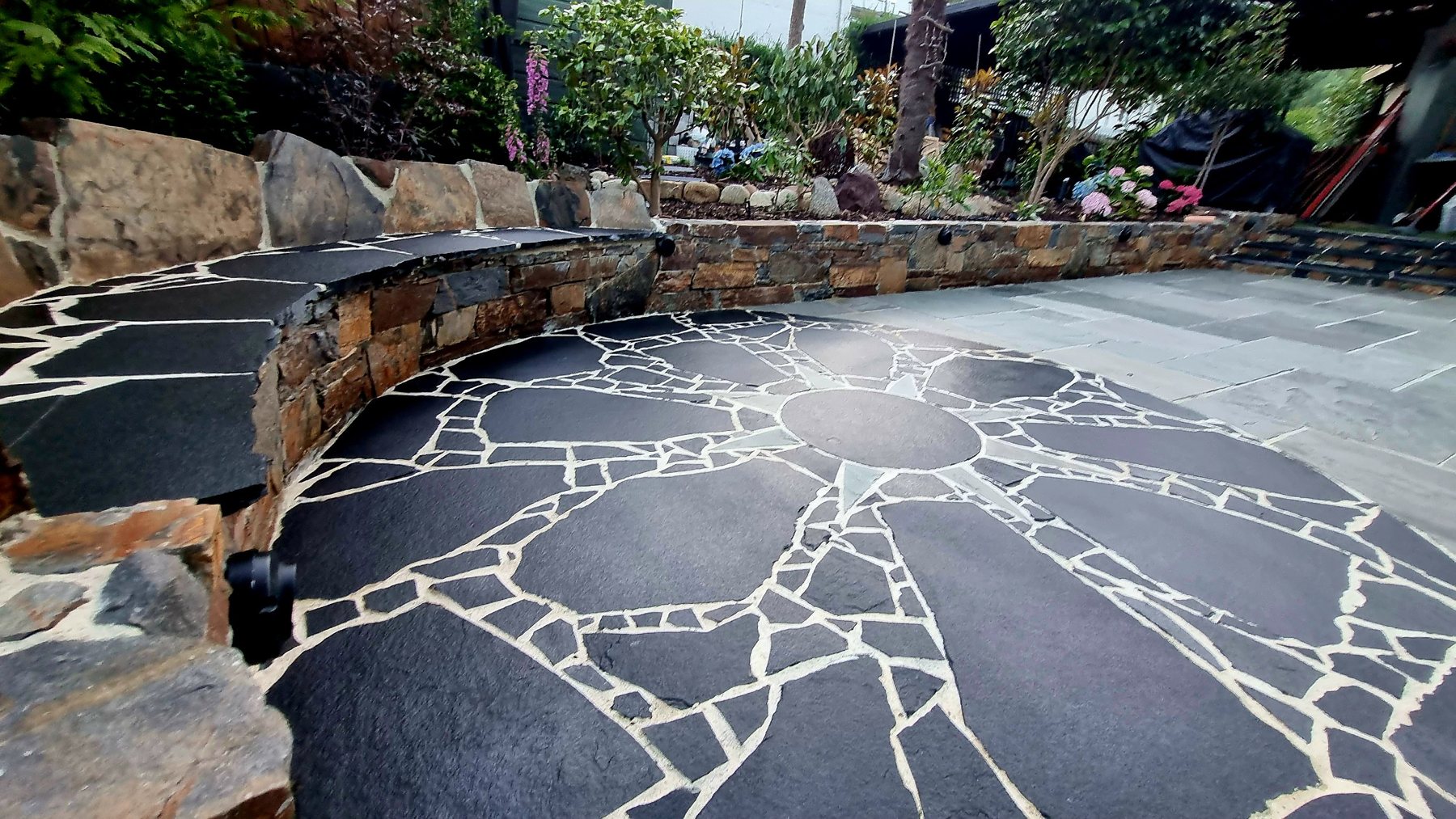 Close view of the black crazy paving sun and the curved stacked stone seat wall