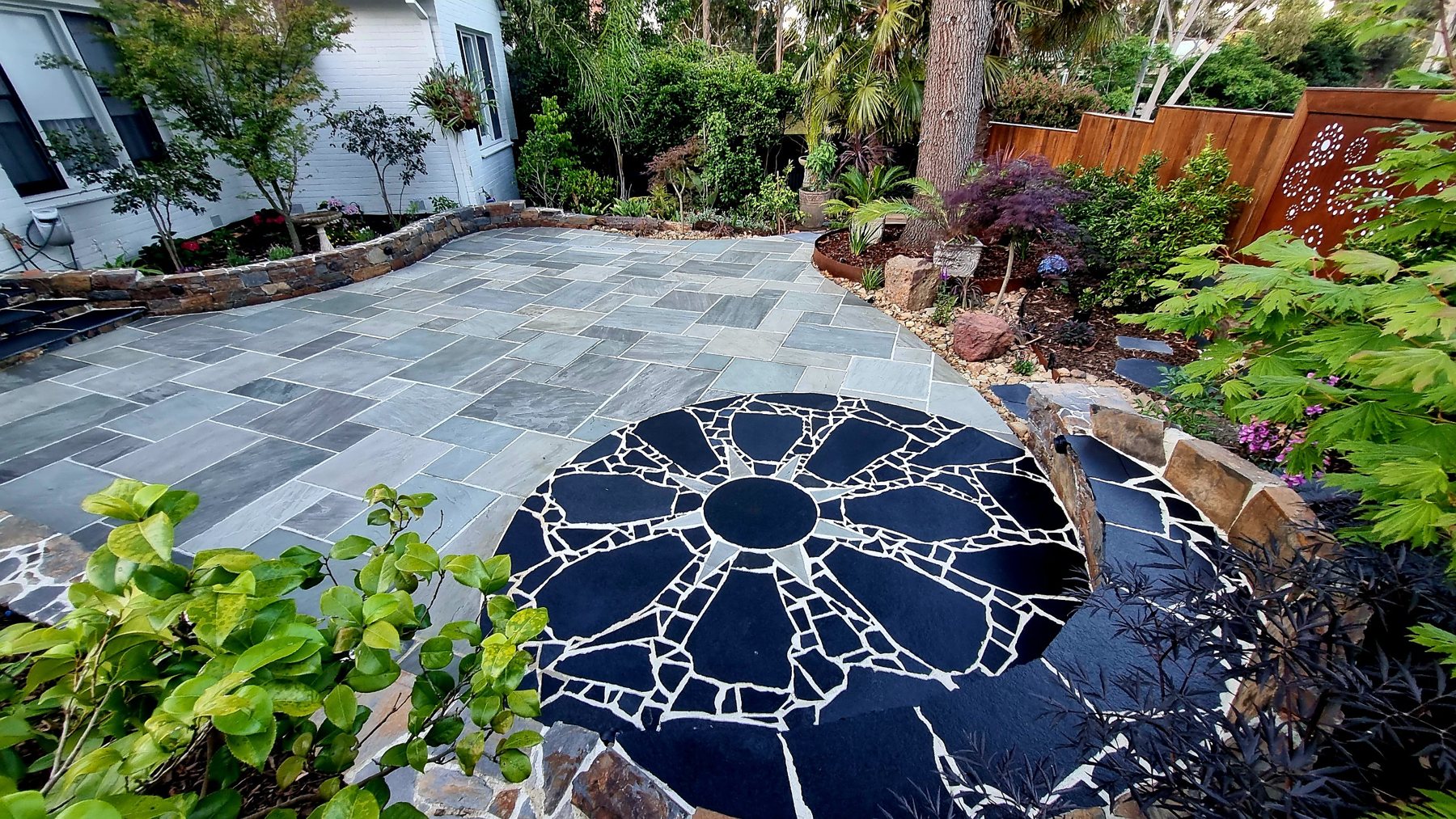 Eight-point sun in black crazy paving set into grey stone paving, wrapped by a curved stone seat wall