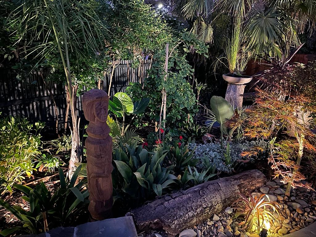 Carved timber totem and log edging among lit planting at night