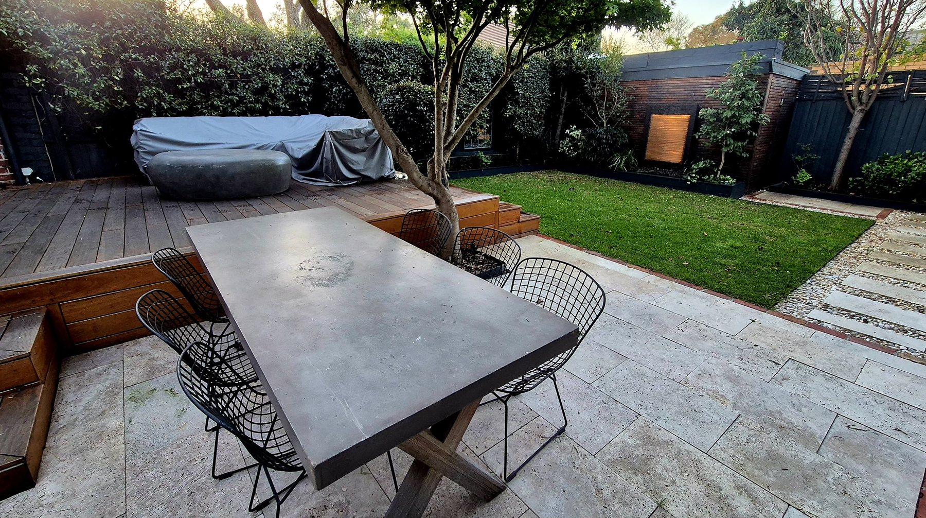 Concrete dining table on travertine, with the lawn and shed water feature behind