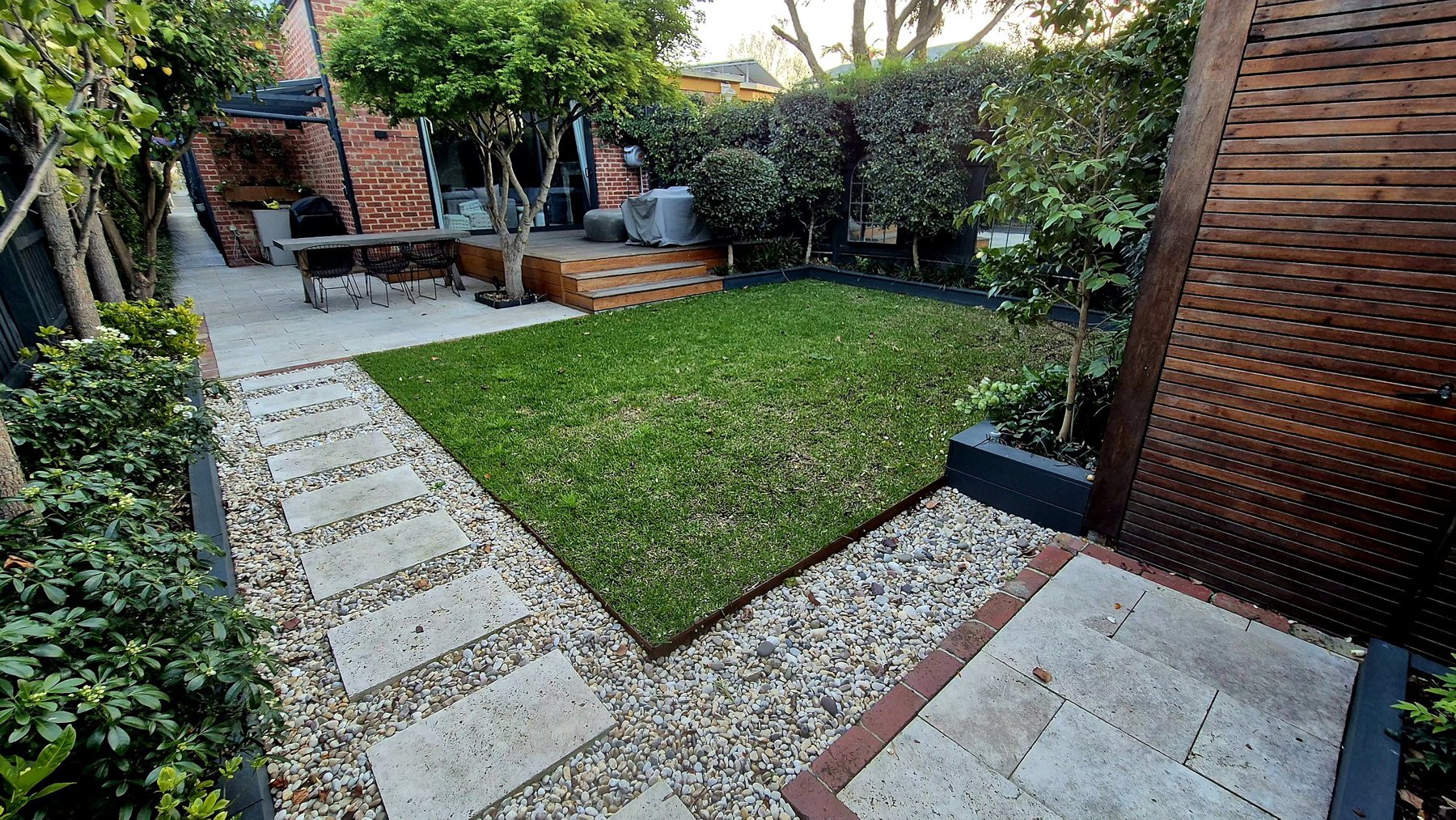 Lawn edged in Corten with travertine stepping stones through river pebbles, toward the hardwood deck