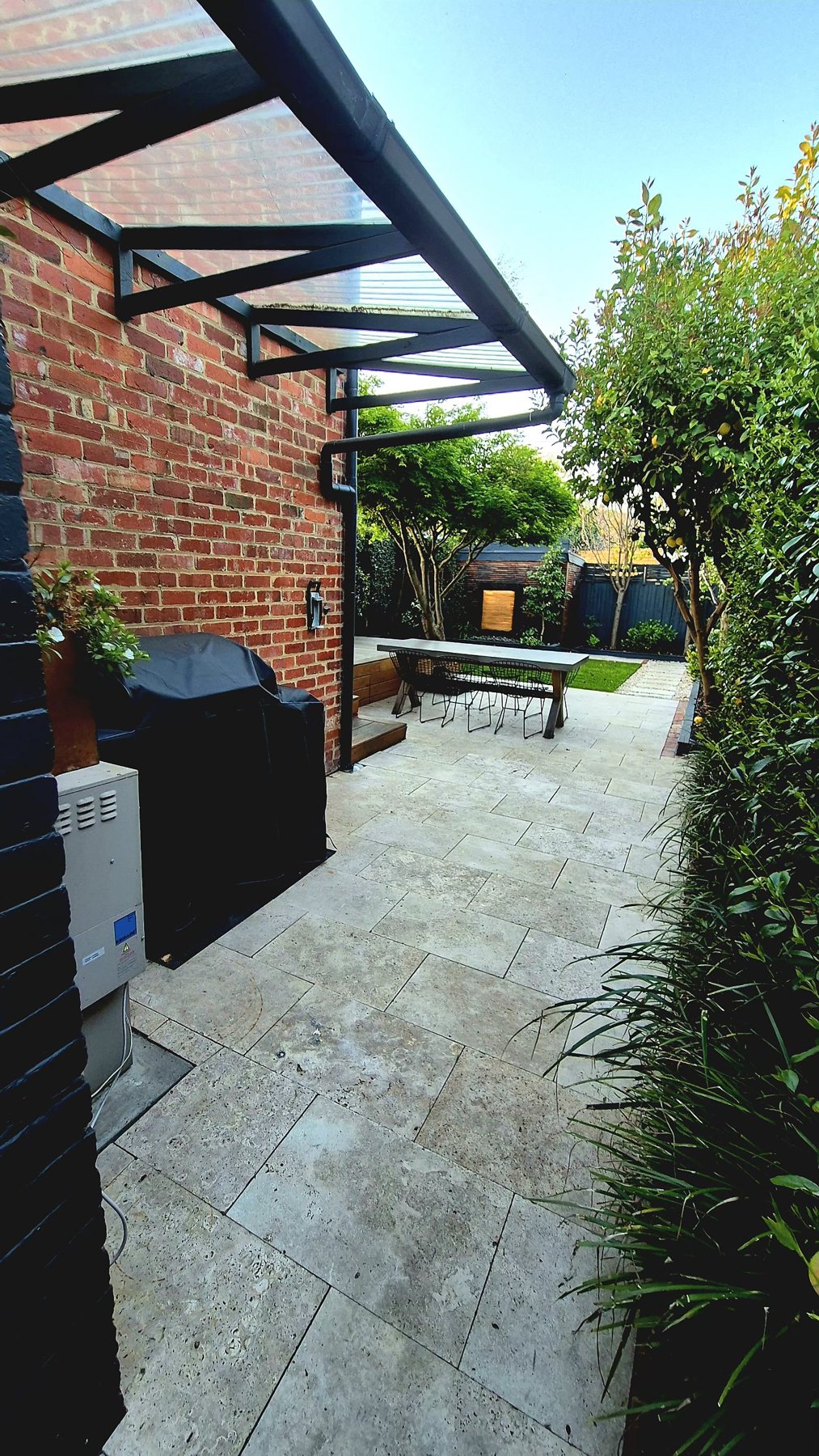 Travertine side terrace under a polycarbonate awning toward the garden
