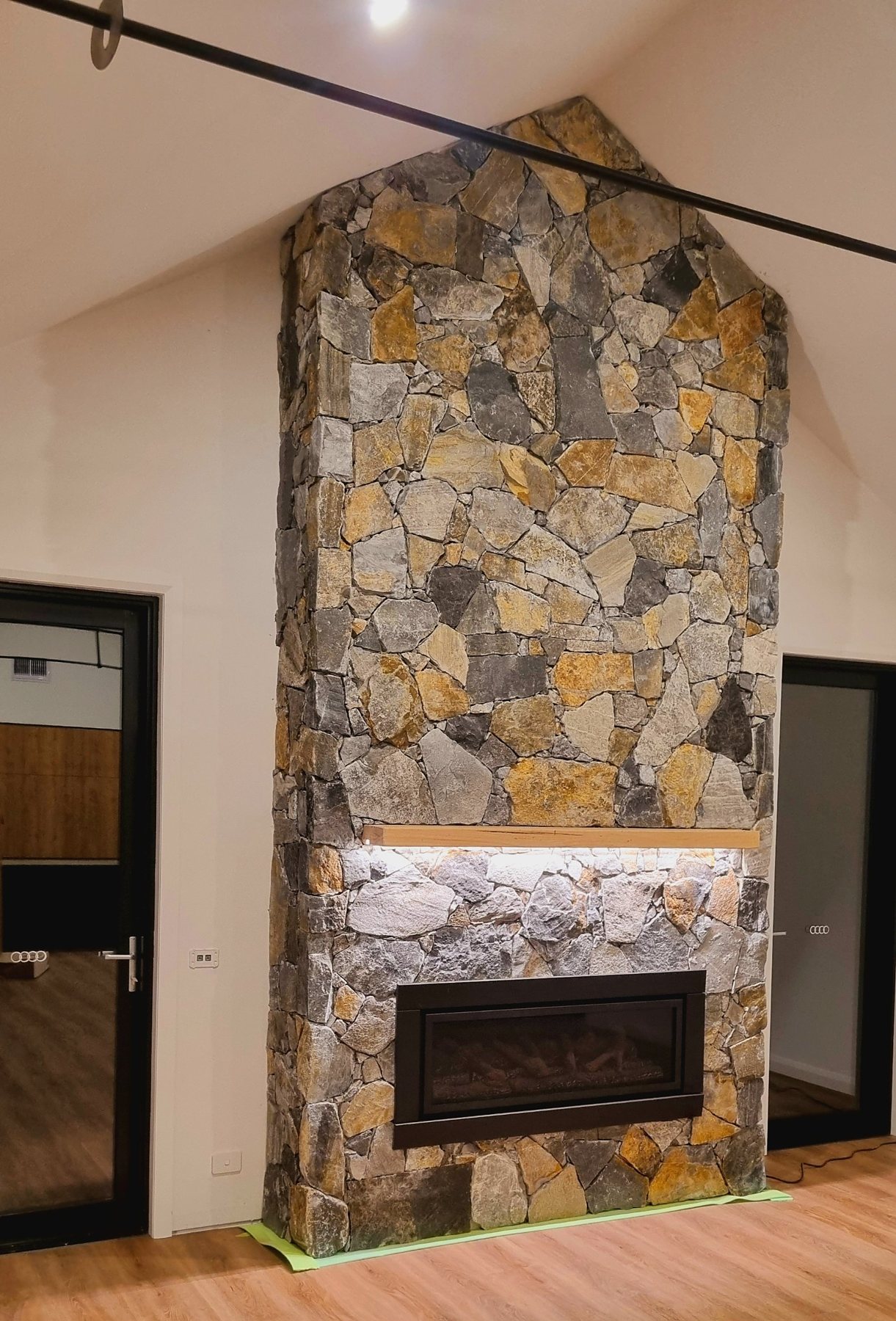 Natural stone fireplace rising into the gable between two black doors, with a timber mantel