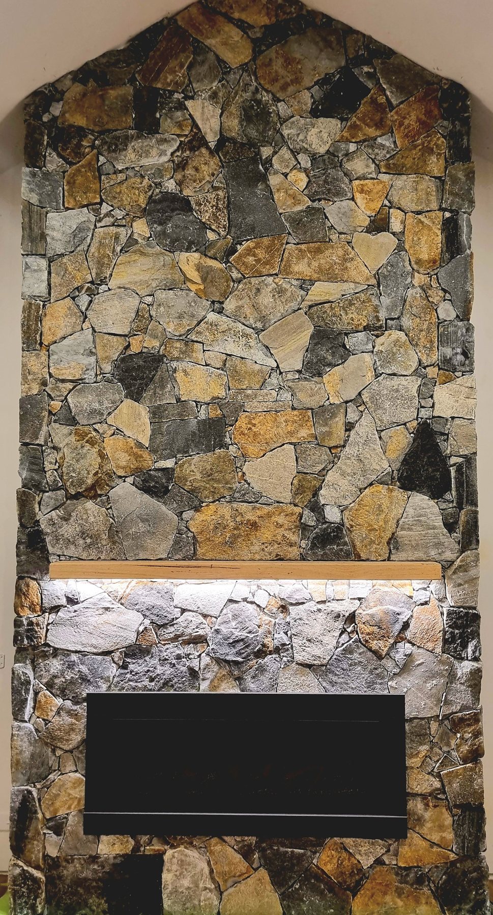 Floor-to-gable natural stone fireplace with a timber mantel and LED strip
