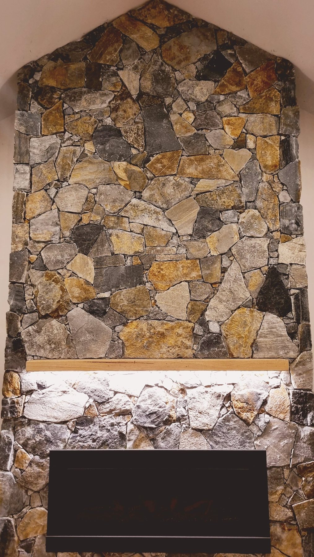 Natural stone fireplace in rust, gold and charcoal stone, peaking into the vaulted ceiling