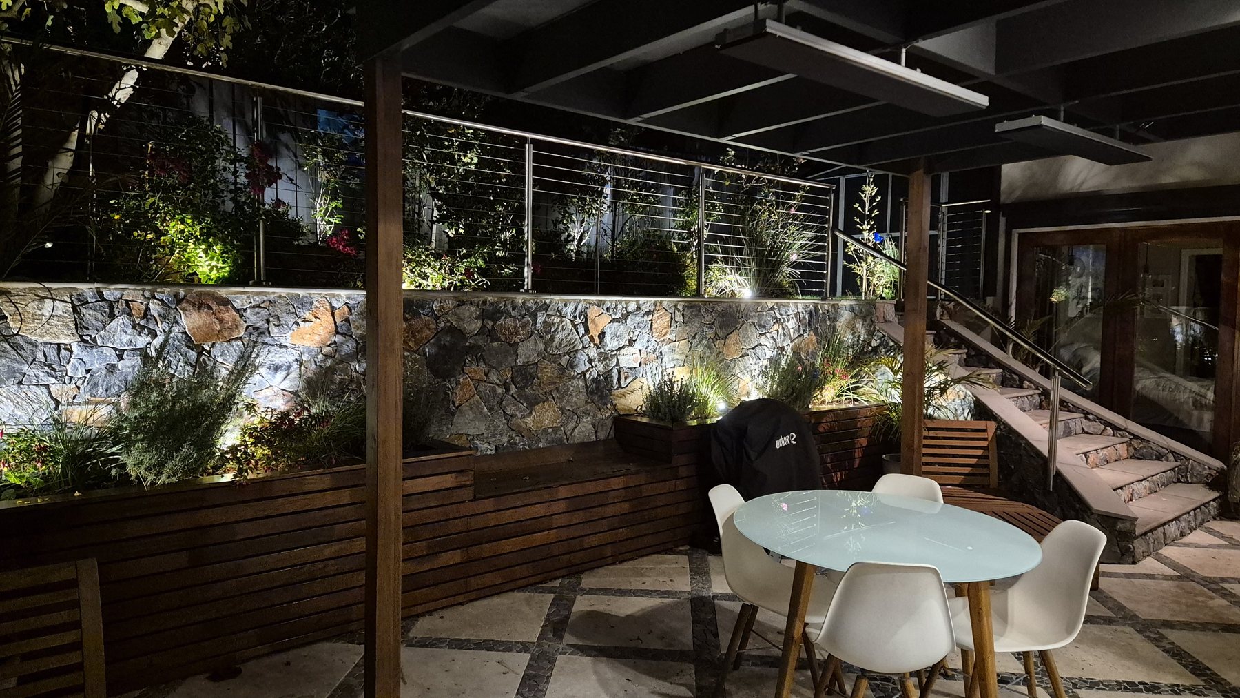Natural stone retaining wall, timber planter benches and garden lighting at night