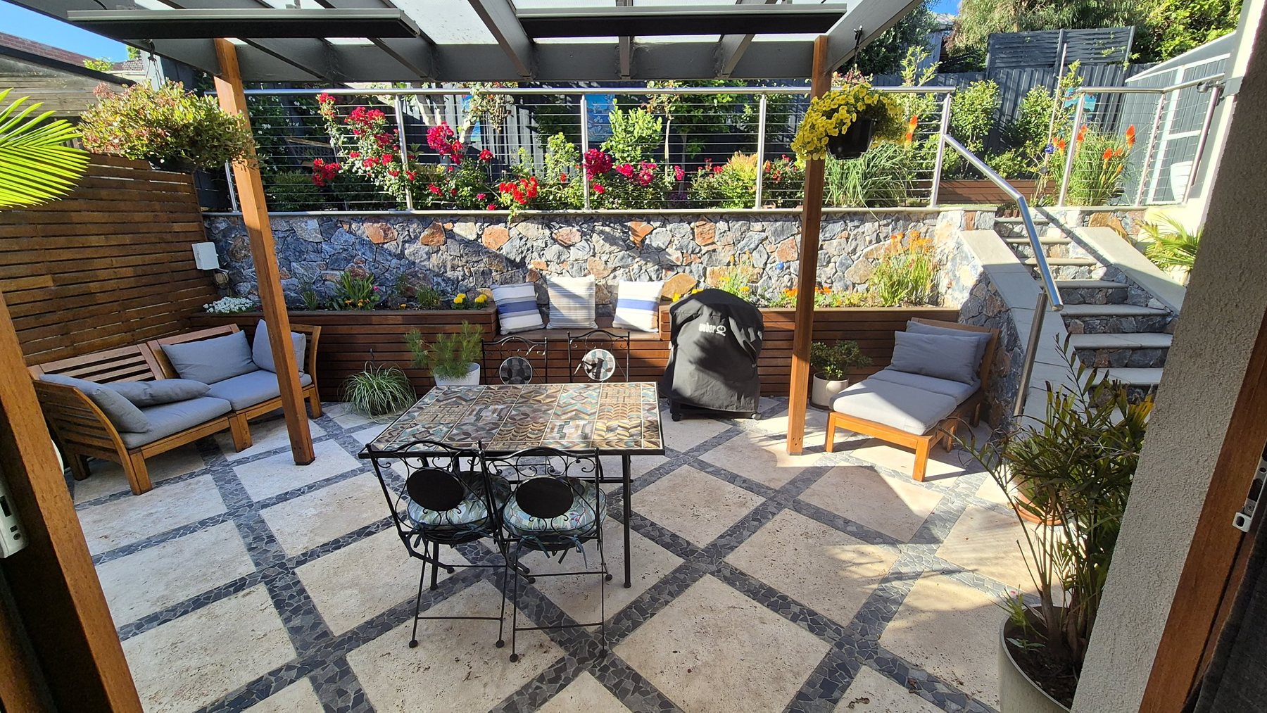 Travertine courtyard under a timber pergola with planter benches and a stone wall