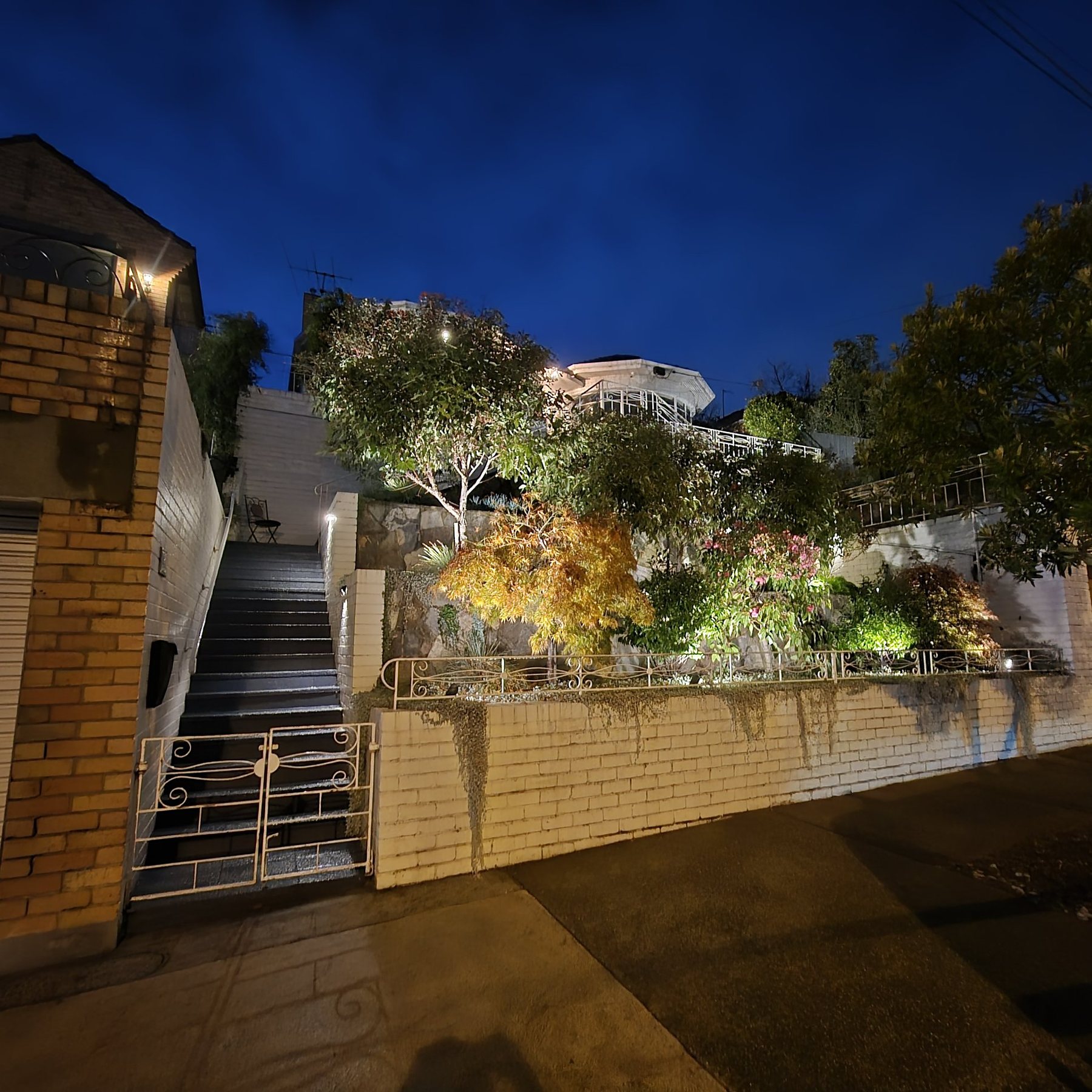 Front garden terraces lit at night above a white brick wall and iron gate