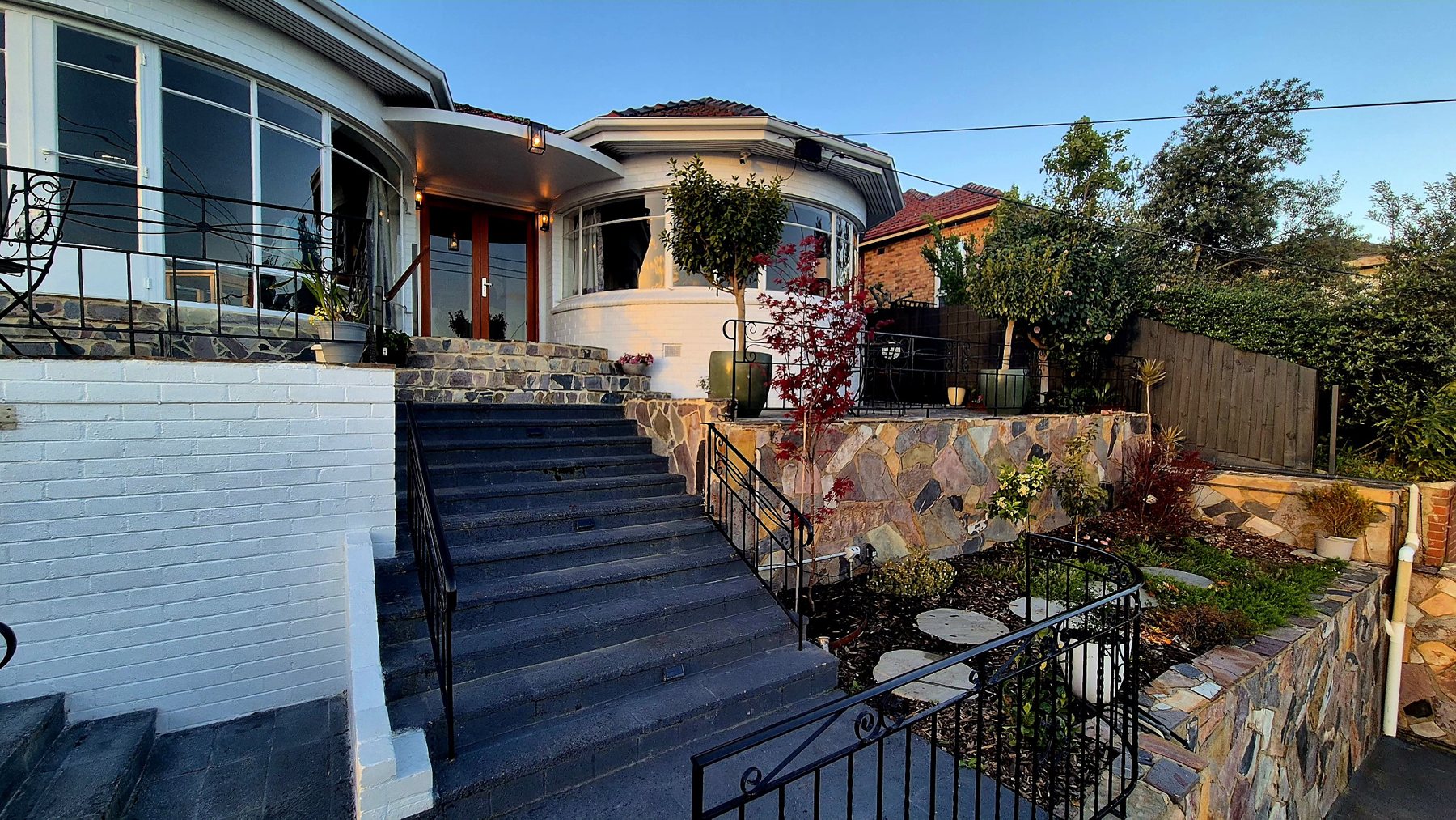 Front steps rising between a white brick wall and natural stone walls to the house