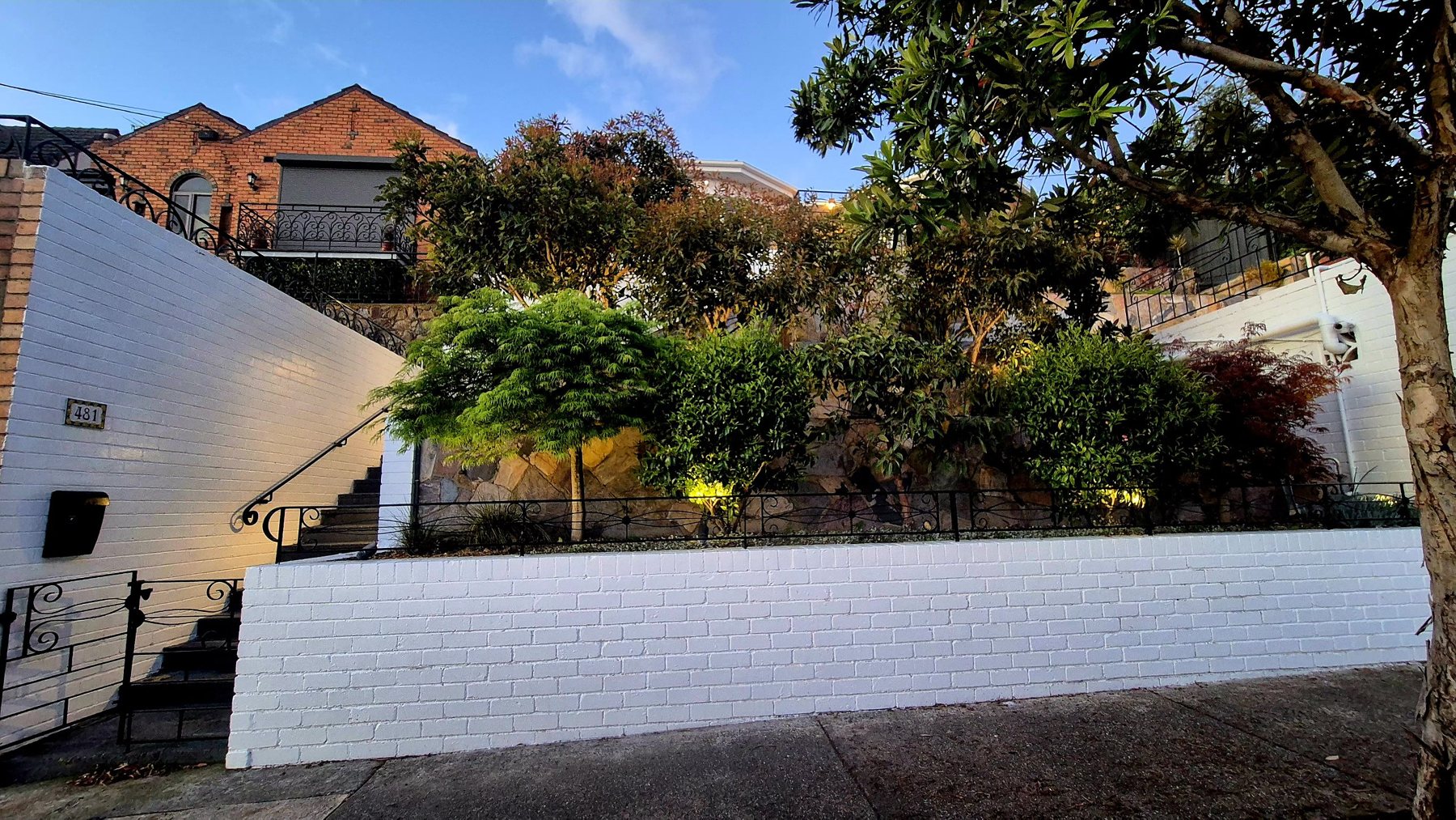 White brick front wall and iron fence below terraced planting and stone walls