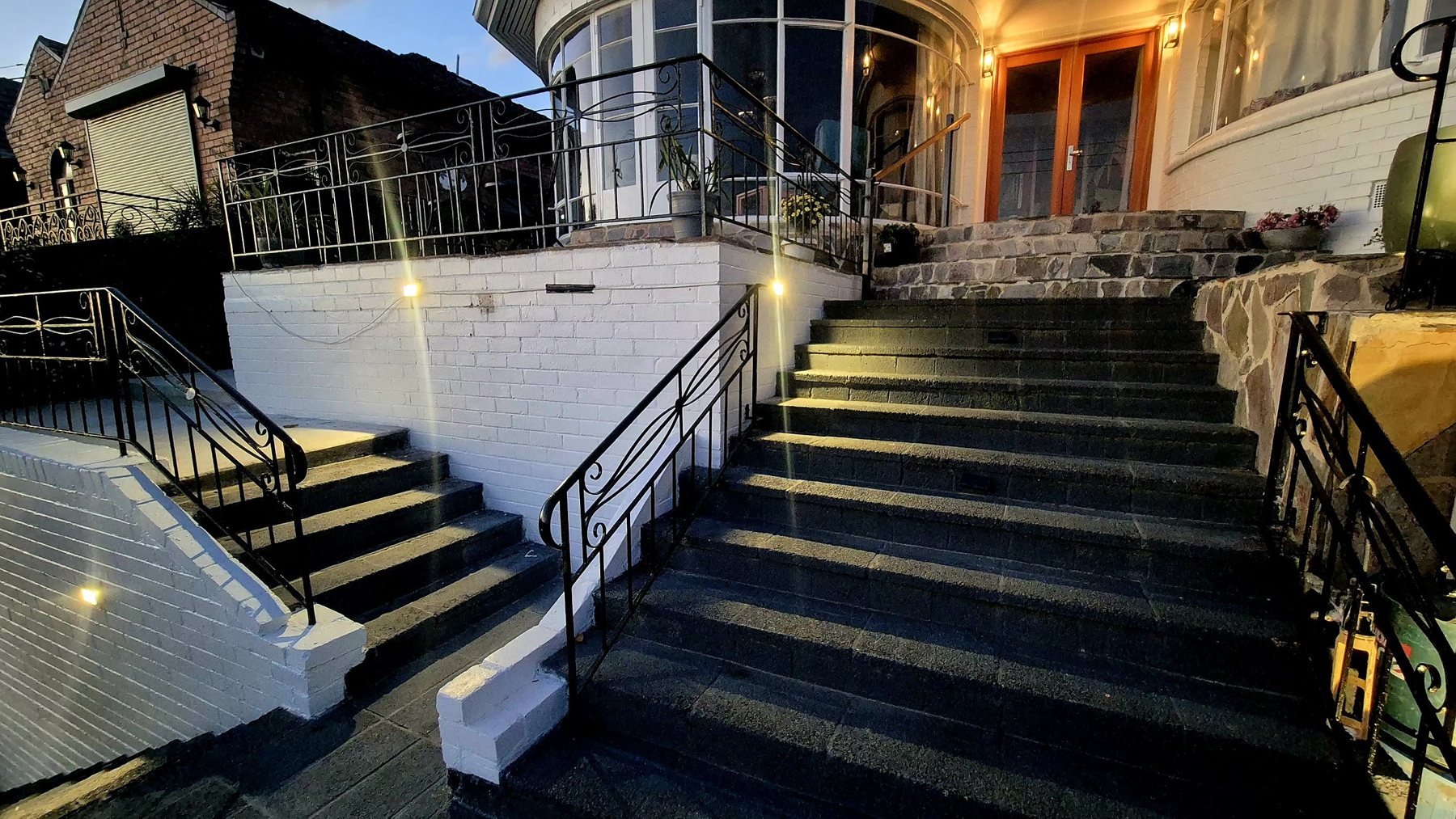Lit entry stairs with iron balustrades up to the house at dusk