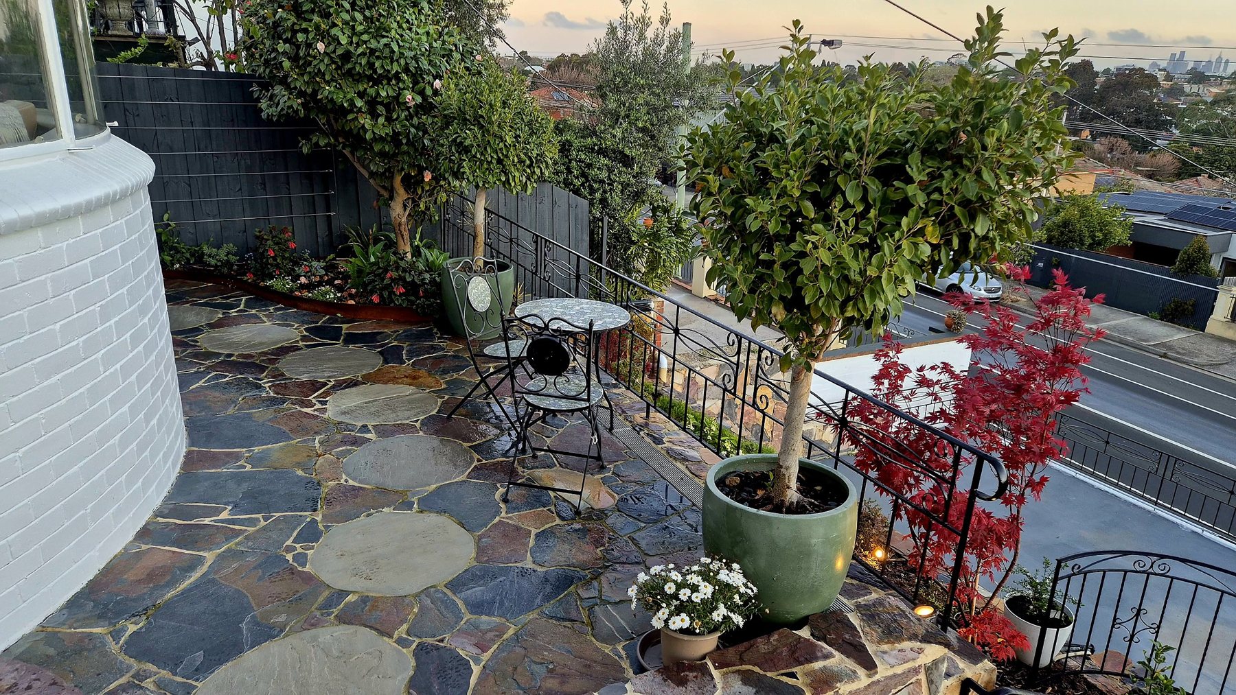 Flagstone terrace with round stepping pavers, potted standards and a red maple above the street
