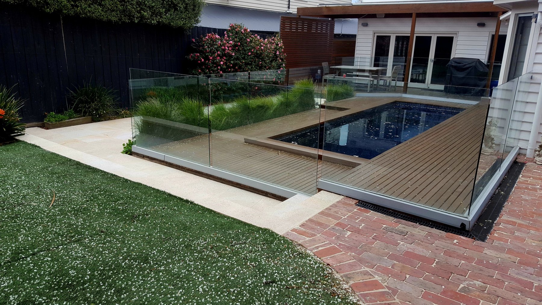 Dark pool with a hardwood deck, frameless glass and brick paving
