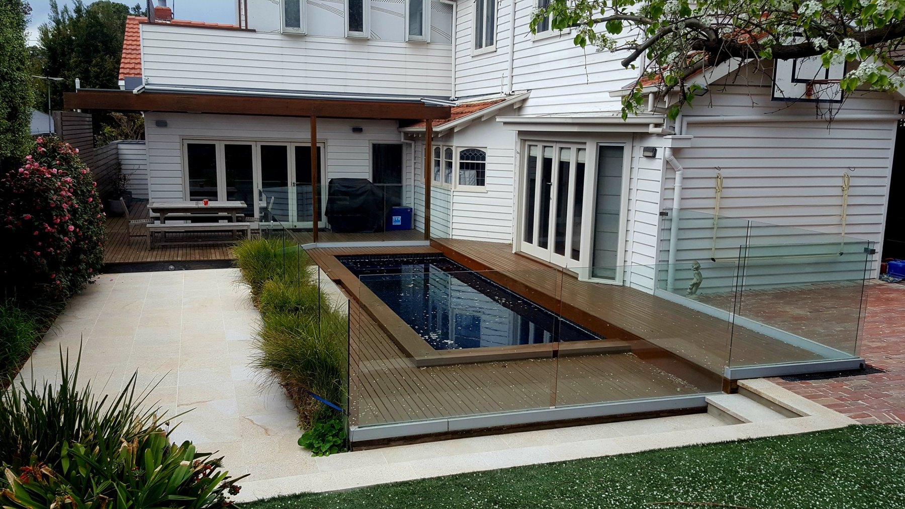 Dark pool with hardwood deck and glass fence behind a weatherboard house