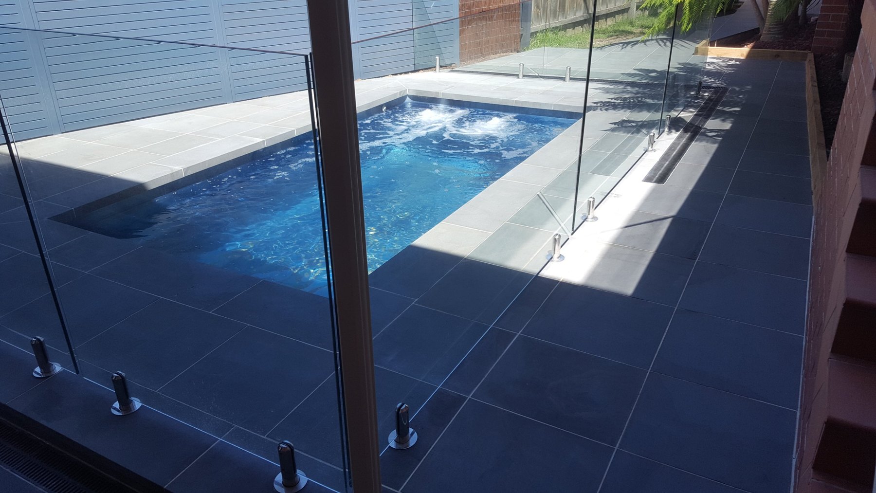 Pool behind frameless glass with dark stone paving