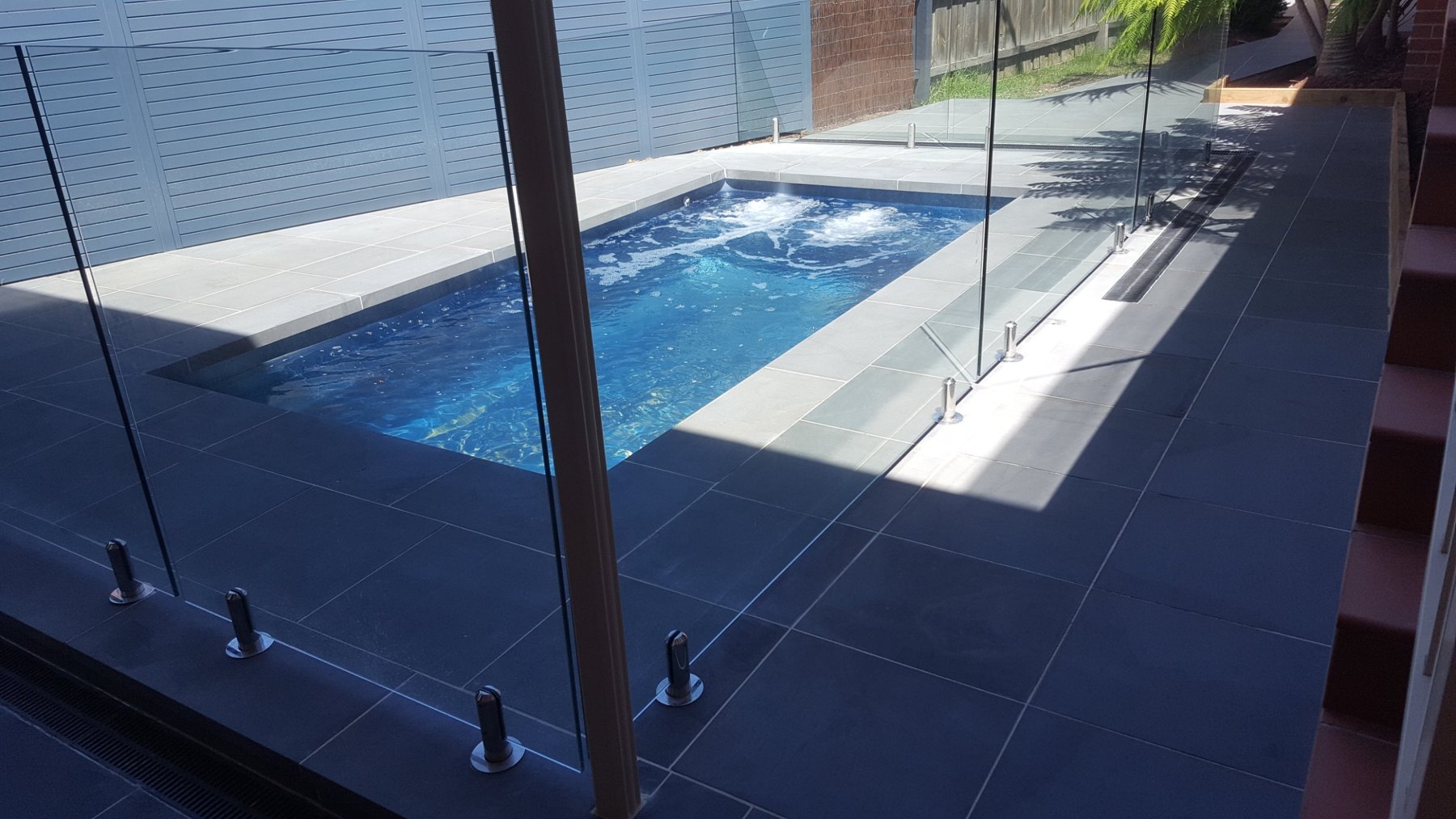 Pool behind frameless glass with dark stone paving