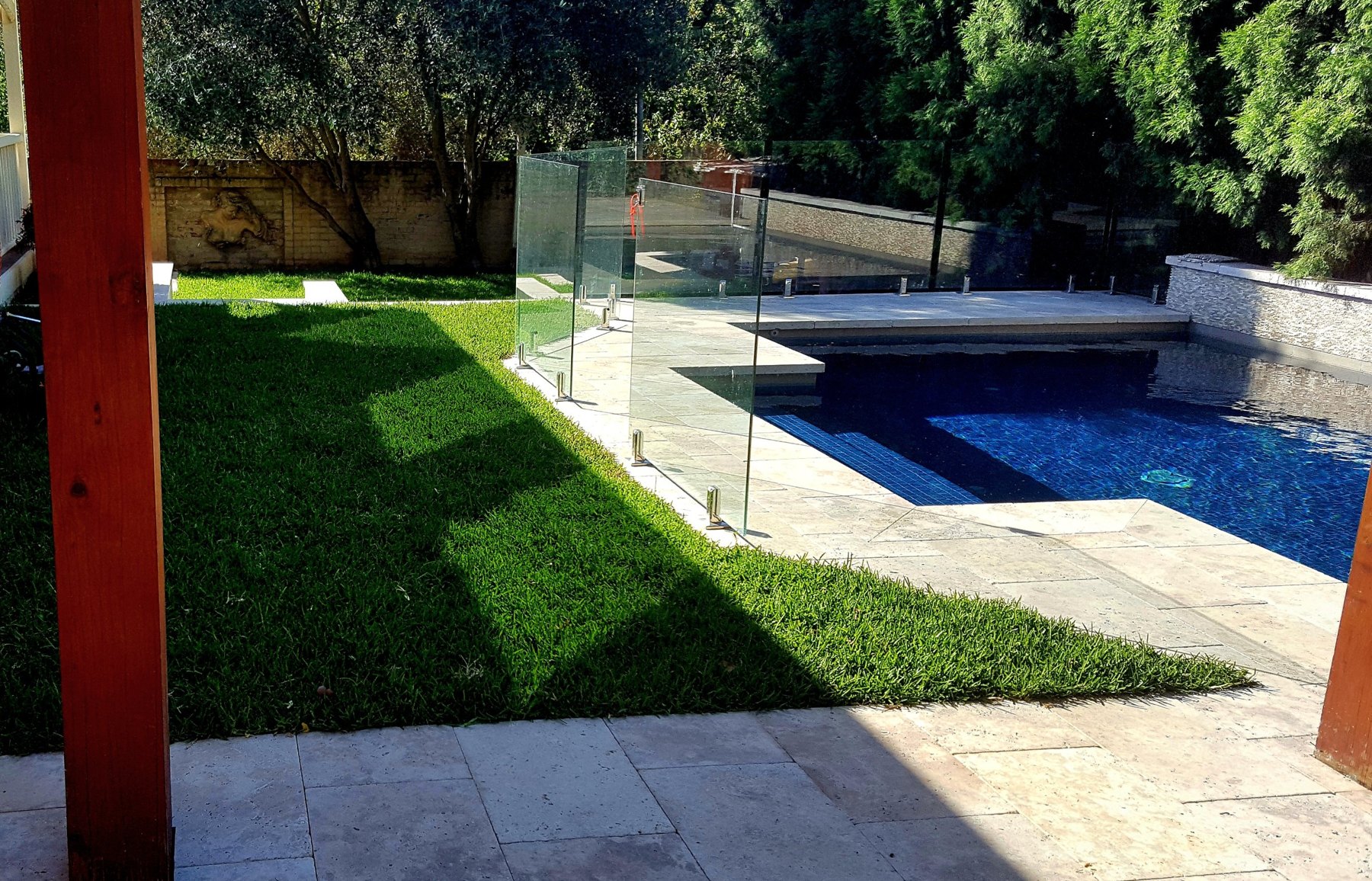 Pool behind frameless glass with lawn and timber pergola posts