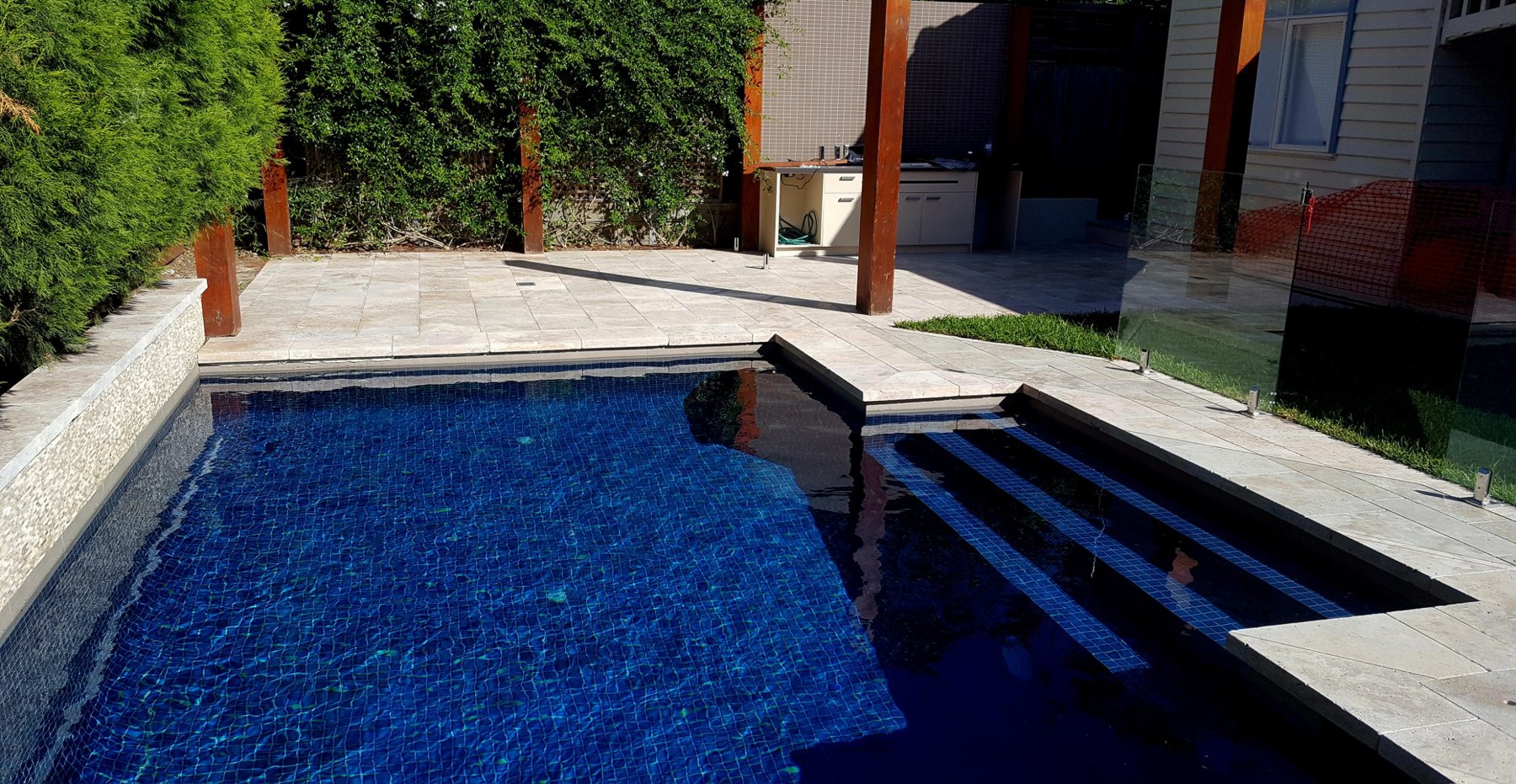 Pool with entry steps and natural stone paving under timber posts