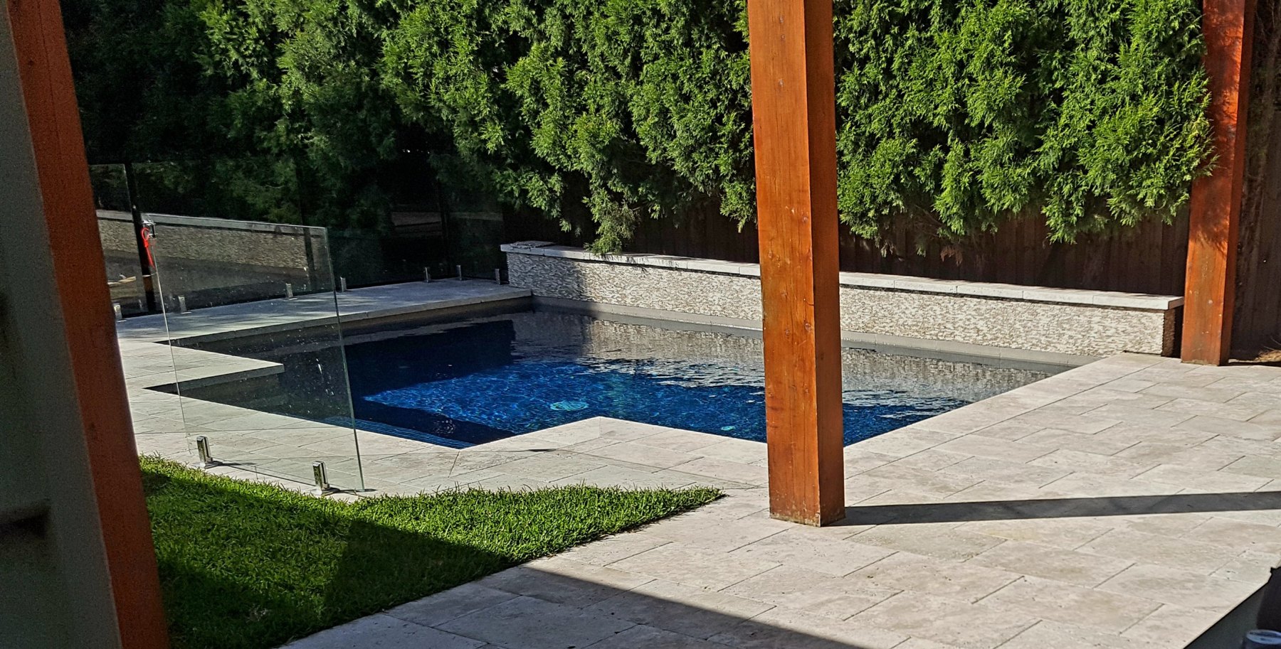 Wide view of the pool, glass fence and paving under timber posts
