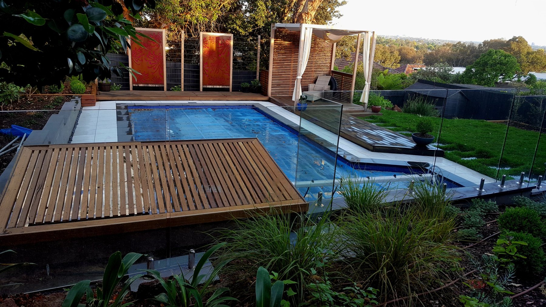 Pool with a slatted timber cover deck and a cabana beyond