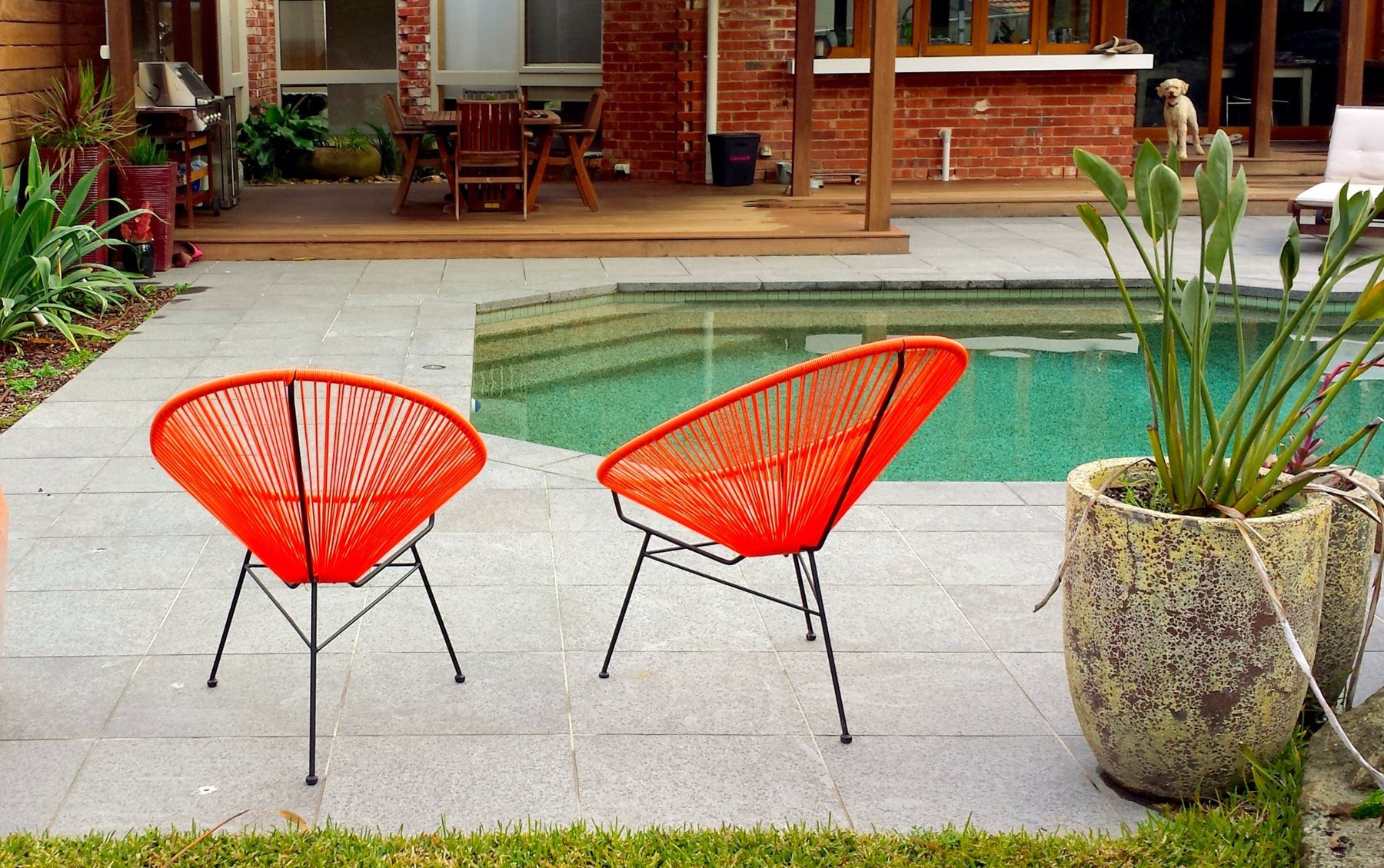 Pool surrounded by stone paving with orange chairs