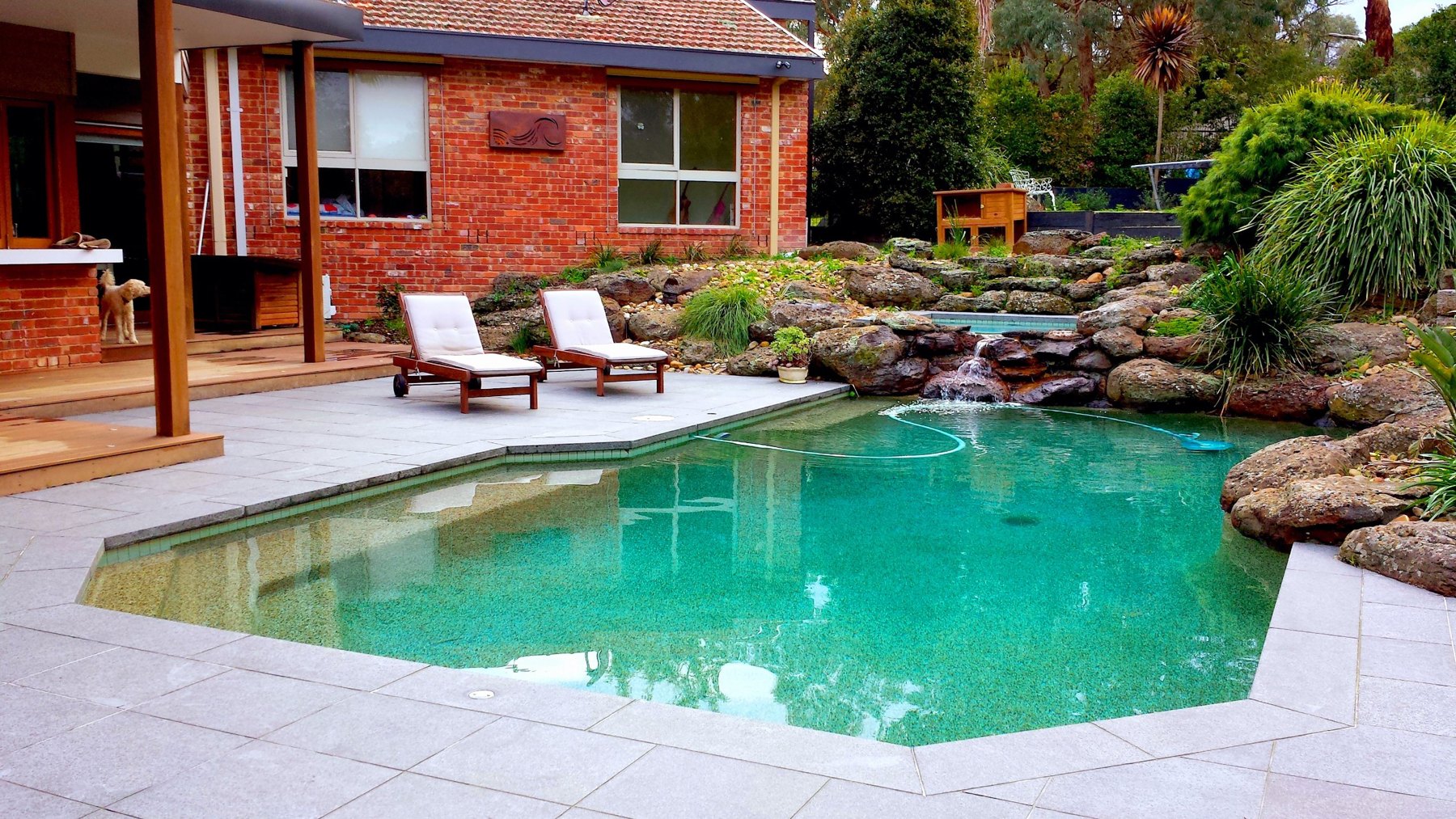 Freeform pool with stone paving, boulders and a waterfall