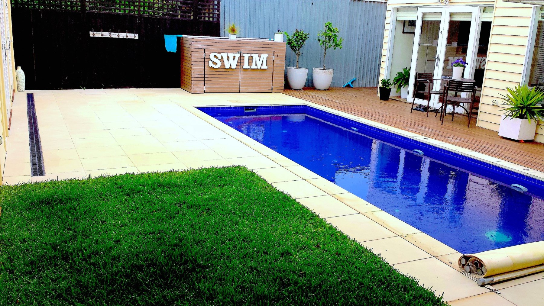 Pool with pale stone coping, lawn and a timber deck beside a SWIM sign