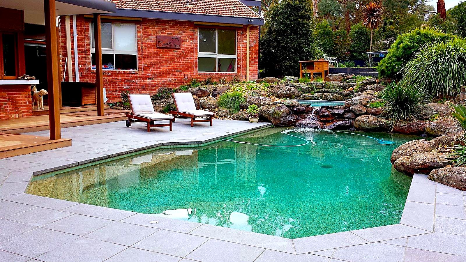 Swimming pool edged with natural boulders and a spa waterfall