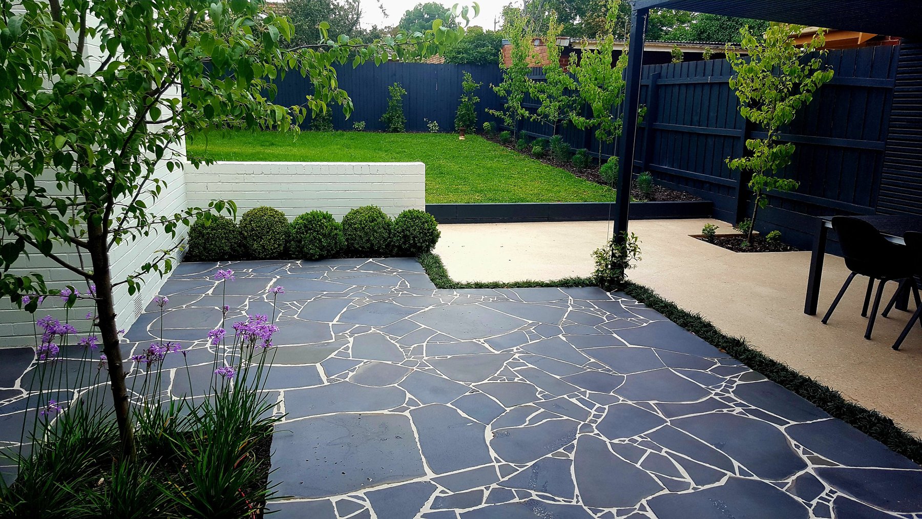 Crazy paving terrace, buxus balls and a raised lawn behind a white brick wall