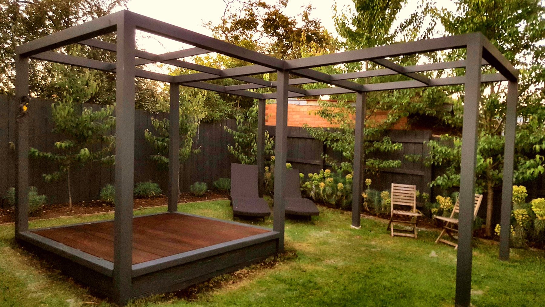 Black timber pergola over a hardwood daybed deck on the lawn