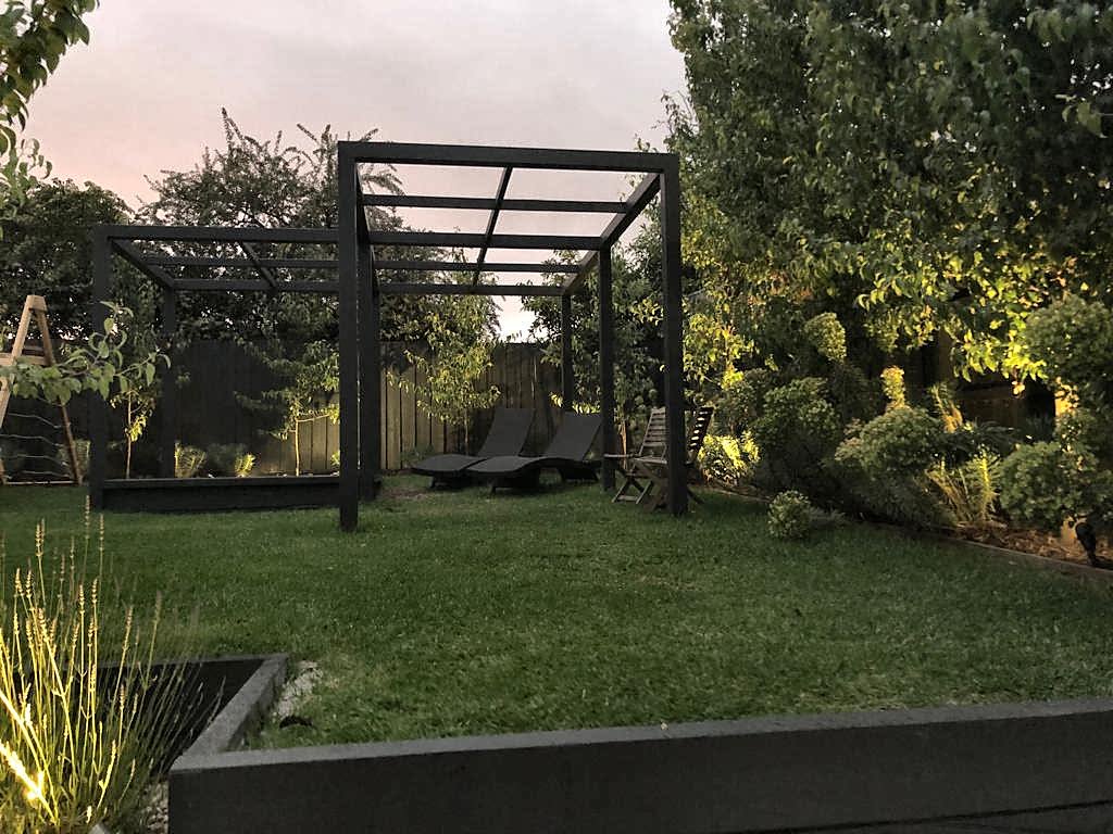 Black pergola and lawn with garden lighting at dusk