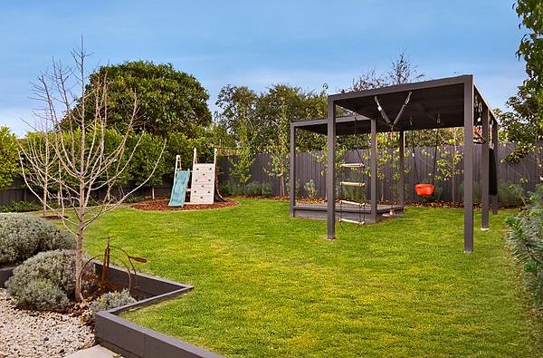 Lawn with a black timber play frame, steel garden bed edging and planting