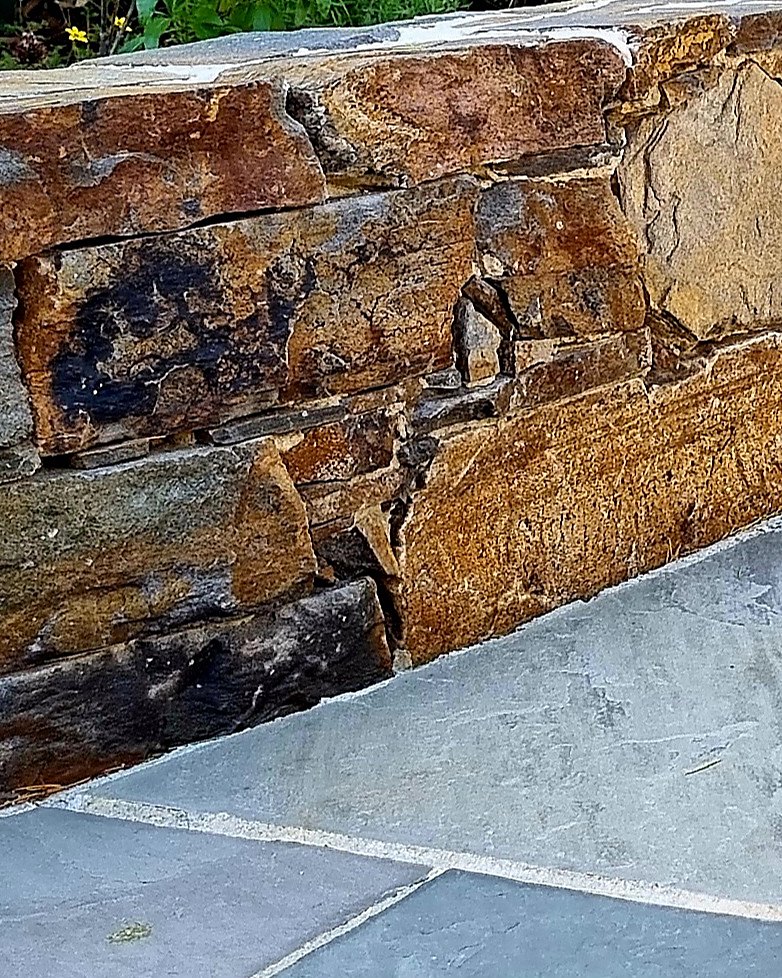 Natural stone seat wall in rust and gold stone above grey stone paving